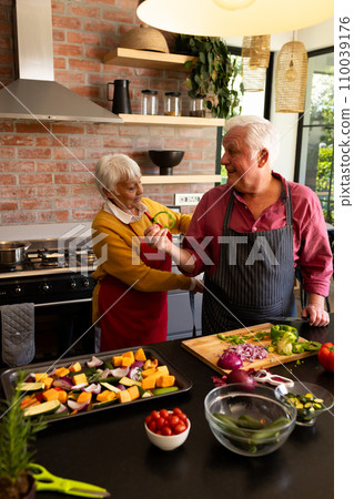 Happy caucasian senior couple putting on aprons, preparing vegetables in kitchen, copy space 110039176