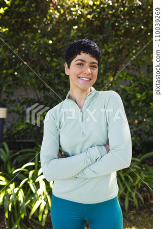 Portrait of happy biracial woman with short dark hair crossing arms and smiling in sunny garden Portrait of happy biracial woman with short dark hair crossing arms and smiling in sunny garden 110039269