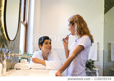 Happy biracial lesbian couple in bathroom brushing teeth and talking in the morning 110039334