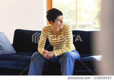 Sad biracial woman sitting on sofa in sunny living room at home Sad biracial woman sitting on sofa in sunny living room at home 110039433