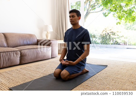 Biracial man doing yoga and meditating at home 110039530