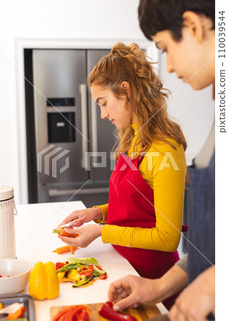 Focused biracial lesbian couple peeling and chopping vegetables in kitchen at home 110039544