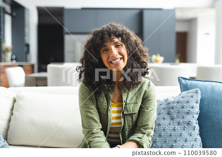 Happy mature caucasian woman having video call, smiling and listening on couch in sunny living room 110039580