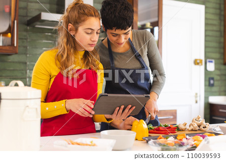 Focused biracial lesbian couple using tablet and preparing vegetables in kitchen Focused biracial lesbian couple using tablet and preparing vegetables in kitchen 110039593