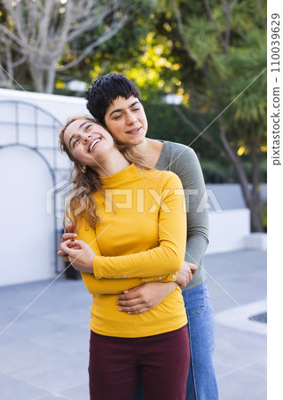 Happy biracial lesbian couple standing on garden terrace embracing and smiling Happy biracial lesbian couple standing on garden terrace embracing and smiling 110039629