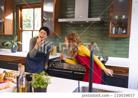 Happy biracial lesbian couple preparing meal having fun singing in kitchen 110039657