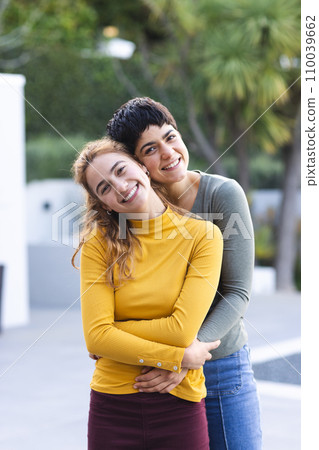 Portrait of biracial lesbian couple standing on garden terrace embracing and smiling, copy space 110039662