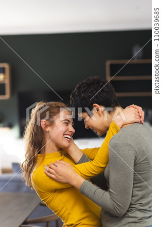 Happy biracial lesbian couple embracing and smiling in kitchen at home, copy space 110039685