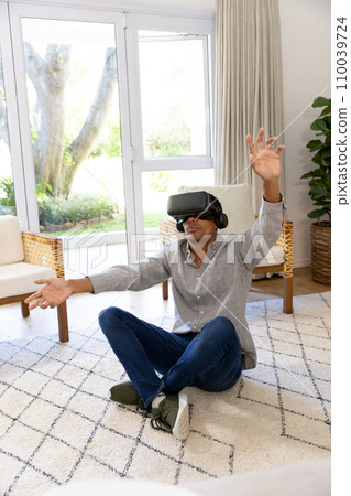 Biracial man using vr headset touching virtual screen at home 110039724