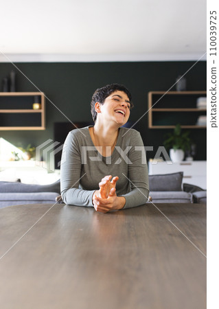 Happy biracial woman sitting at dining table having video call at home, laughing, copy space 110039725
