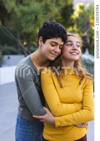 Happy biracial lesbian couple standing on garden terrace embracing and smiling 110039764