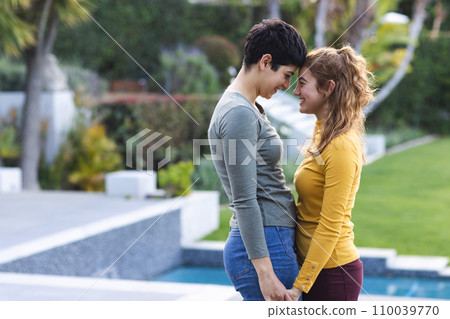 Happy biracial lesbian couple on garden terrace holding hands and touching heads, copy space 110039770