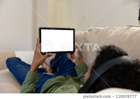 Biracial man lying on sofa using tablet with copy space on screen at home 110039777