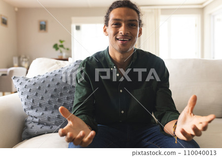 Happy biracial man with long curly hair having video call in sunny living room at home Happy biracial man with long curly hair having video call in sunny living room at home 110040013