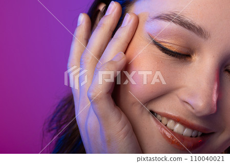Caucasian woman wearing eyeliner and lip gloss on purple background Caucasian woman wearing eyeliner and lip gloss on purple background 110040021