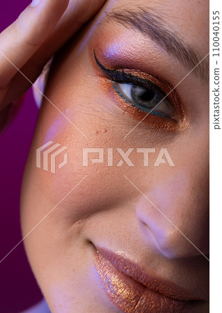Portrait of caucasian woman wearing golden eye shadow and lipstick on purple background 110040155
