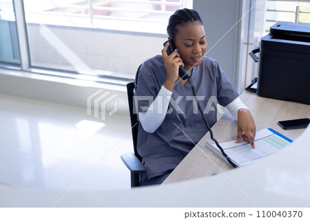Happy african american female doctor talking on phone in hospital reception 110040370