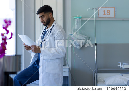 Biracial male doctor reading document in sunny hospital room Biracial male doctor reading document in sunny hospital room 110040510