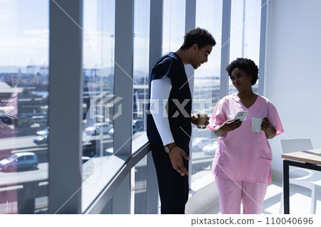 Happy diverse male and female doctors talking, drinking coffee and using smartphone in hospital 110040696