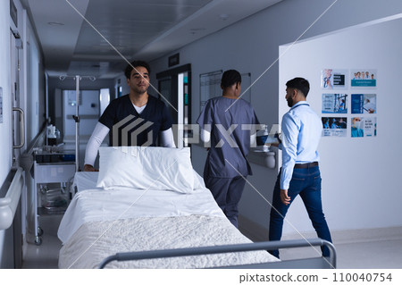 Biracial male doctor walking with bed in hospital corridor Biracial male doctor walking with bed in hospital corridor 110040754