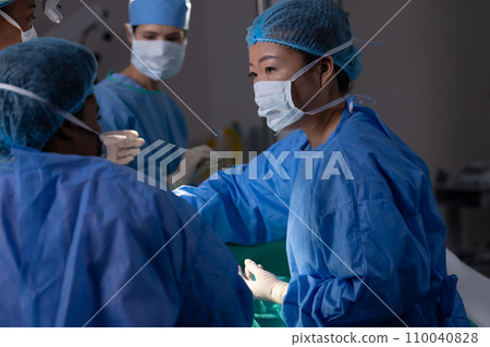 Diverse female doctors with face masks doing surgery in hospital operating room 110040828