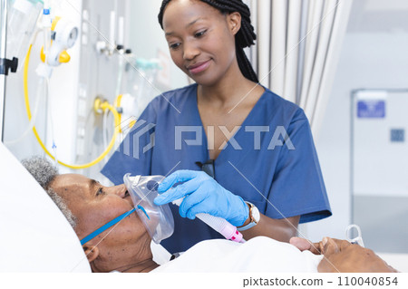 African american female doctor applying oxygen mask to senior female patient in hospital room 110040854