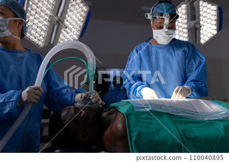 Diverse female doctors with face masks doing surgery in hospital operating room Diverse female doctors with face masks doing surgery in hospital operating room 110040895