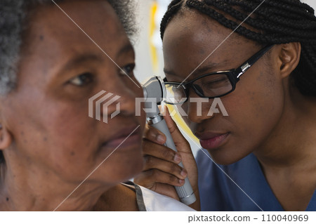 African american female doctor testing ear of senior female patient in hospital room 110040969