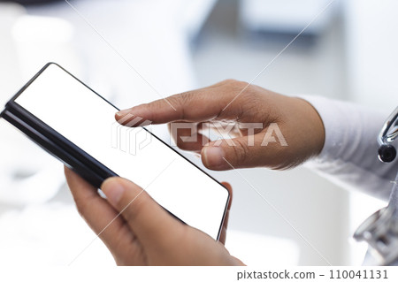Midsection of biracial female doctor wearing scrubs using smartphon with copy space in hospital 110041131