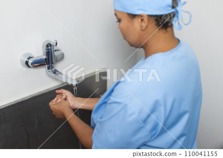 Biracial female doctor wearing scrubs washing hands in operating theatre 110041155