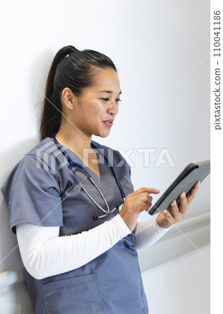 Biracial female doctor wearing scrubs using tablet in hospital corridor Biracial female doctor wearing scrubs using tablet in hospital corridor 110041186