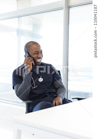 Happy african american male doctor talking on smartphone at desk in hospital Happy african american male doctor talking on smartphone at desk in hospital 110041187