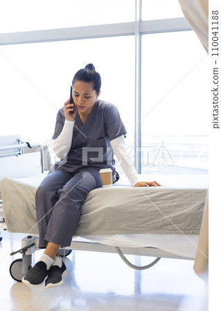 Biracial female doctor talking on smartphone on bed in hospital, copy space 110041188
