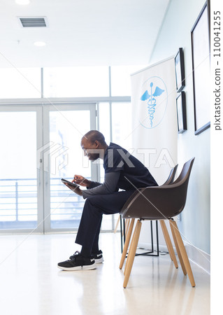 Happy african american male doctor using tablet in waiting room in hospital, copy space 110041255