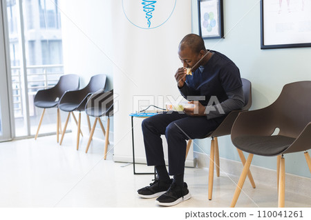 African american male doctor eating takeaway food in waiting room in hospital, copy space 110041261