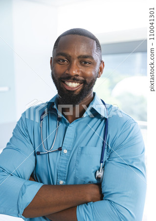 Portrait of happy african american male doctor wearing blue shirt and stethoscope in hospital room Portrait of happy african american male doctor wearing blue shirt and stethoscope in hospital room 110041301