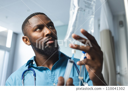 African american male doctor wearing blue shirt applying drip in hospital room African american male doctor wearing blue shirt applying drip in hospital room 110041302