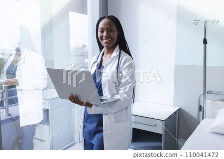 Portrait of happy african american female doctor using laptop in hospital room, copy space 110041472