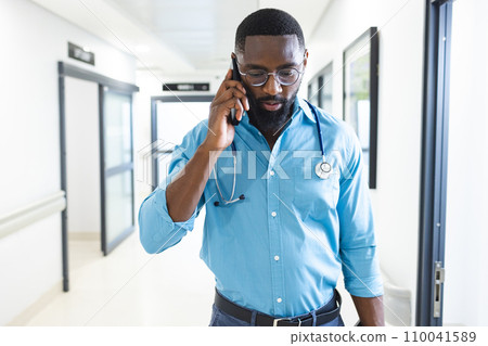 African american male doctor talking on smartphone in corridor in hospital African american male doctor talking on smartphone in corridor in hospital 110041589