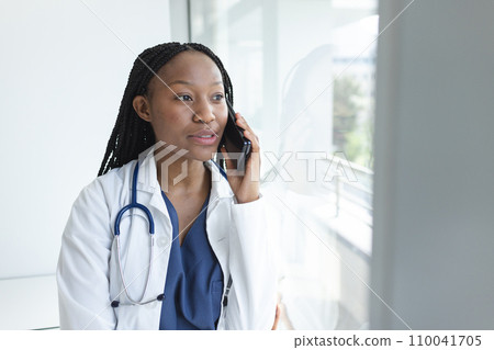 African american female doctor wearing lab coat talking on smartphone in hospital African american female doctor wearing lab coat talking on smartphone in hospital 110041705