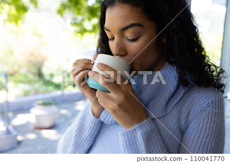 Biracial woman drinking coffee at sunny home Biracial woman drinking coffee at sunny home 110041770