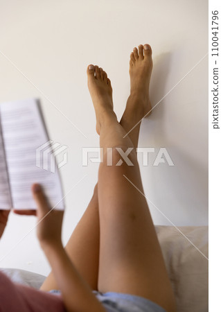 Legs of biracial woman reading book and lying on bed at sunny home 110041796