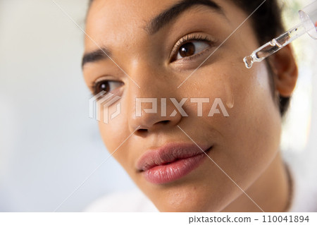 Biracial woman in bathrobe applying cosmetic on her face in sunny bathroom Biracial woman in bathrobe applying cosmetic on her face in sunny bathroom 110041894