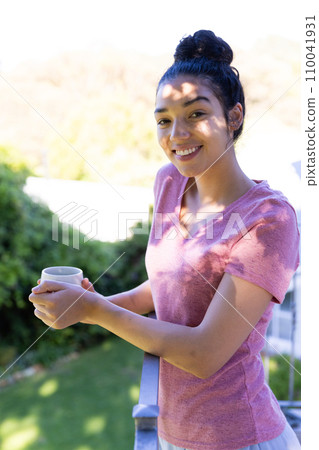 Portrait of happy biracial woman holding cup of coffee on sunny terrace 110041931