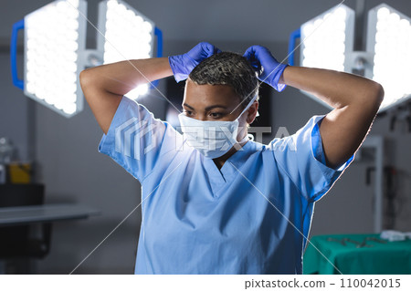 Biracial female surgeon wearing scrubs and face mask in operating theatre 110042015