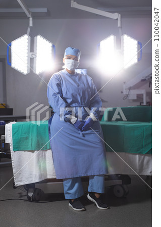 Portrait of biracial female surgeon wearing surgical gown and face mask in operating theatre Portrait of biracial female surgeon wearing surgical gown and face mask in operating theatre 110042047