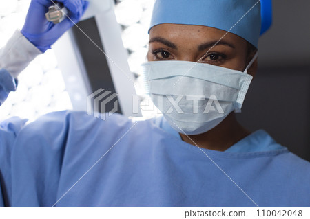 Portrait of biracial female surgeon wearing surgical gown and face mask in operating theatre Portrait of biracial female surgeon wearing surgical gown and face mask in operating theatre 110042048