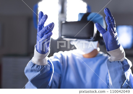 Biracial female surgeon wearing surgical gown using vr headset in operating theatre Biracial female surgeon wearing surgical gown using vr headset in operating theatre 110042049