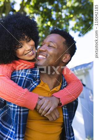 Happy african american couple riding piggyback in sunny garden, copy space 110042185