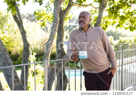 African american senior man holding cup of coffee on sunny terrace 110042317